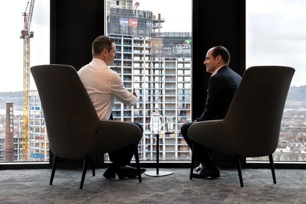António Simões, CEO of Legal & General, seated by a window with a colleague, with construction workers visible outside.
