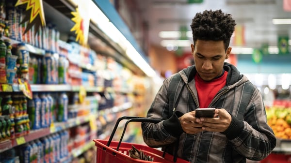 A man looks at his phone as he shops in a supermarket.