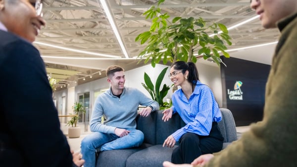 Four people seated on a dark grey circular sofa in Legal & General’s London office. Plants are arranged in the centre of the seating area, behind the people.