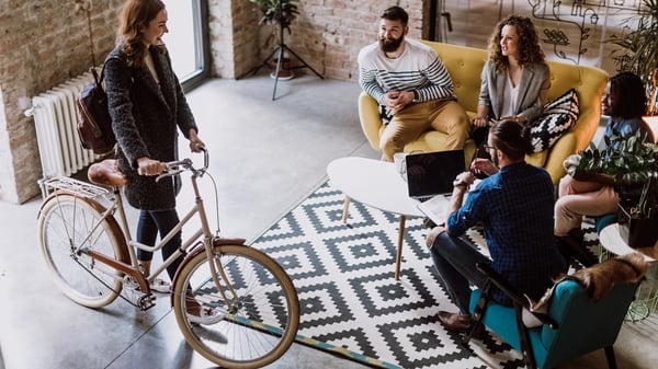 A young woman arrives at a office by bicycle and greets her colleagues.
